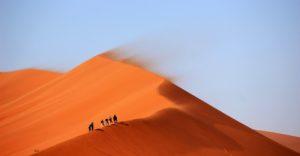 Ihmisiä vaeltamassa kohti vuoren huippua hiekka-aavikolla